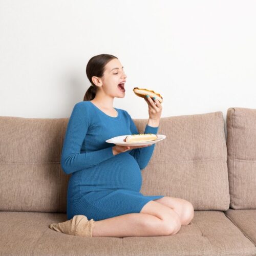 pregnant woman sitting on a couch eating a hot dog