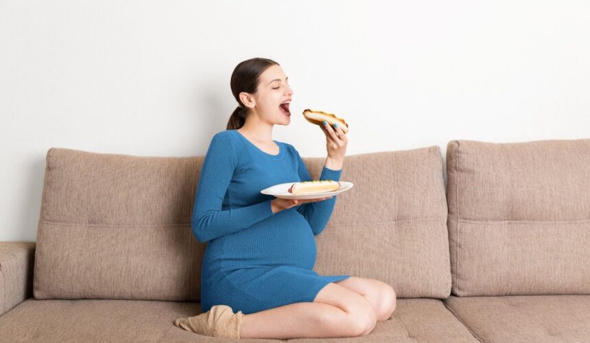 pregnant woman sitting on a couch eating a hot dog