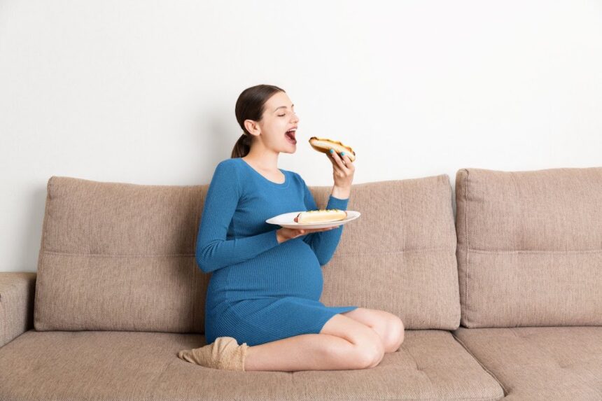 pregnant woman sitting on a couch eating a hot dog
